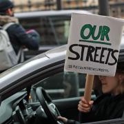 A woman holding a Reclaim the Streets placard out of the passenger window drives past New Scotland Yard in London, the day after clashes between police and crowds who gathered on Clapham Common on Saturday night to remember Sarah Everard. The
